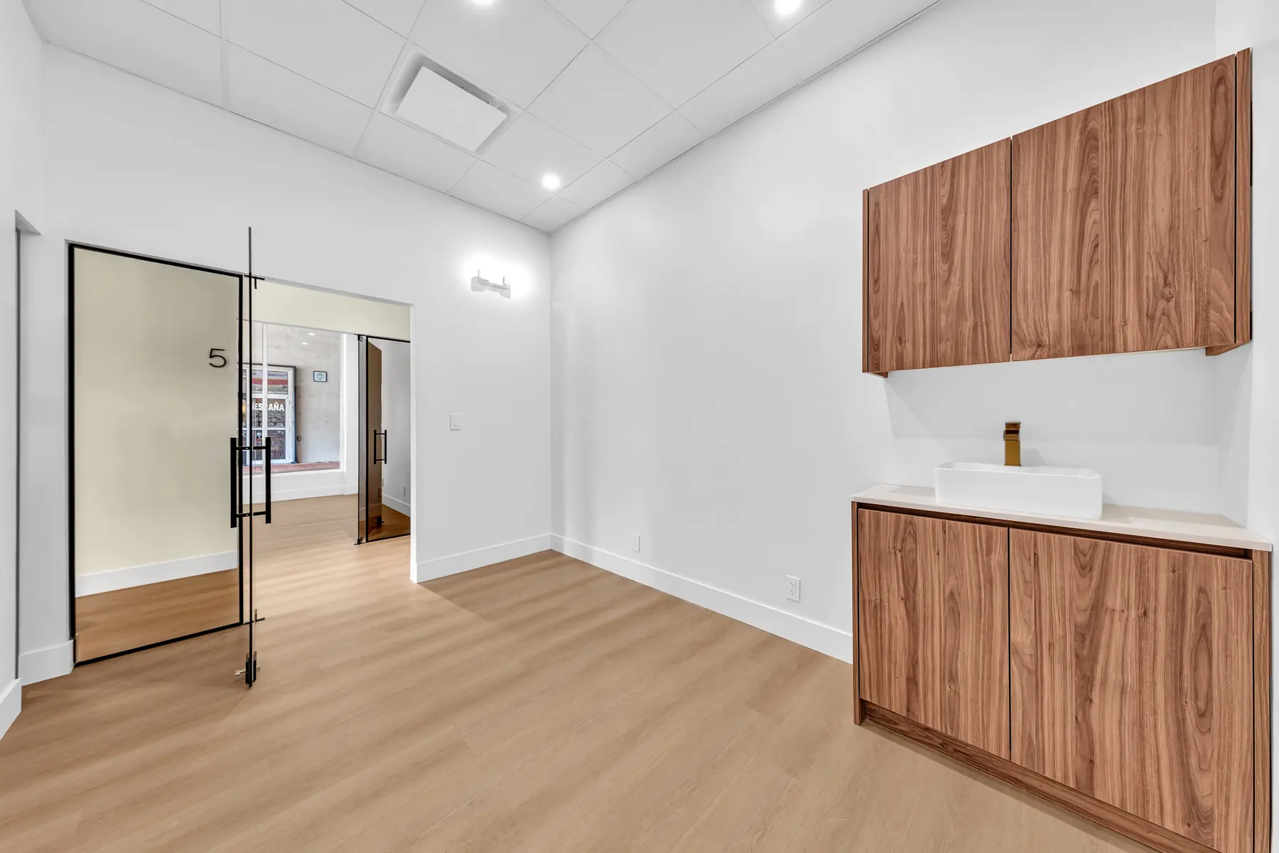Empty suite with walnut cabinets, white countertop and a vessel sink with a brass faucet